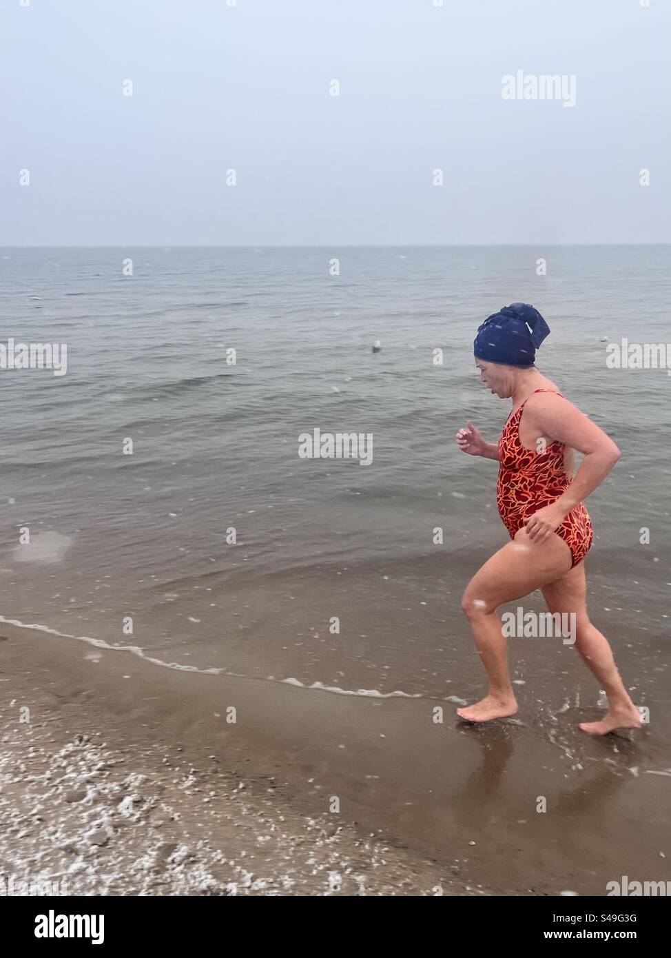 Seule femme nageuse d'hiver en maillot de bain lumineux jogging le long du bord de mer à la plage de Gdansk de la mer Baltique lors d'une chute de neige à Gdansk, Pologne, Europe, UE - Image de stock capturée avec un smartphone Seule femme nageuse d'hiver en maillot de bain lumineux jogging le long du bord de mer à la plage de Gdansk de la mer Baltique lors d'une chute de neige à Gdansk, Pologne, Europe, UE - Image de stock capturée avec un smartphone