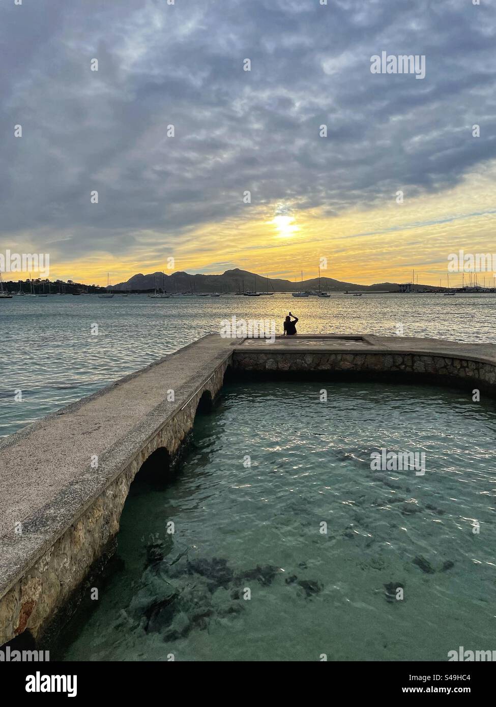 Femme assise sur un quai et prenant des photos du soleil levant à Port de Polença, Majorque, Espagne Banque D'Images