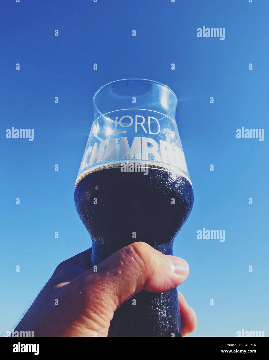 Main tenant un verre froid de Lord Chambray, Fungus Rock, bière stout, contre le ciel bleu. Banque D'Images
