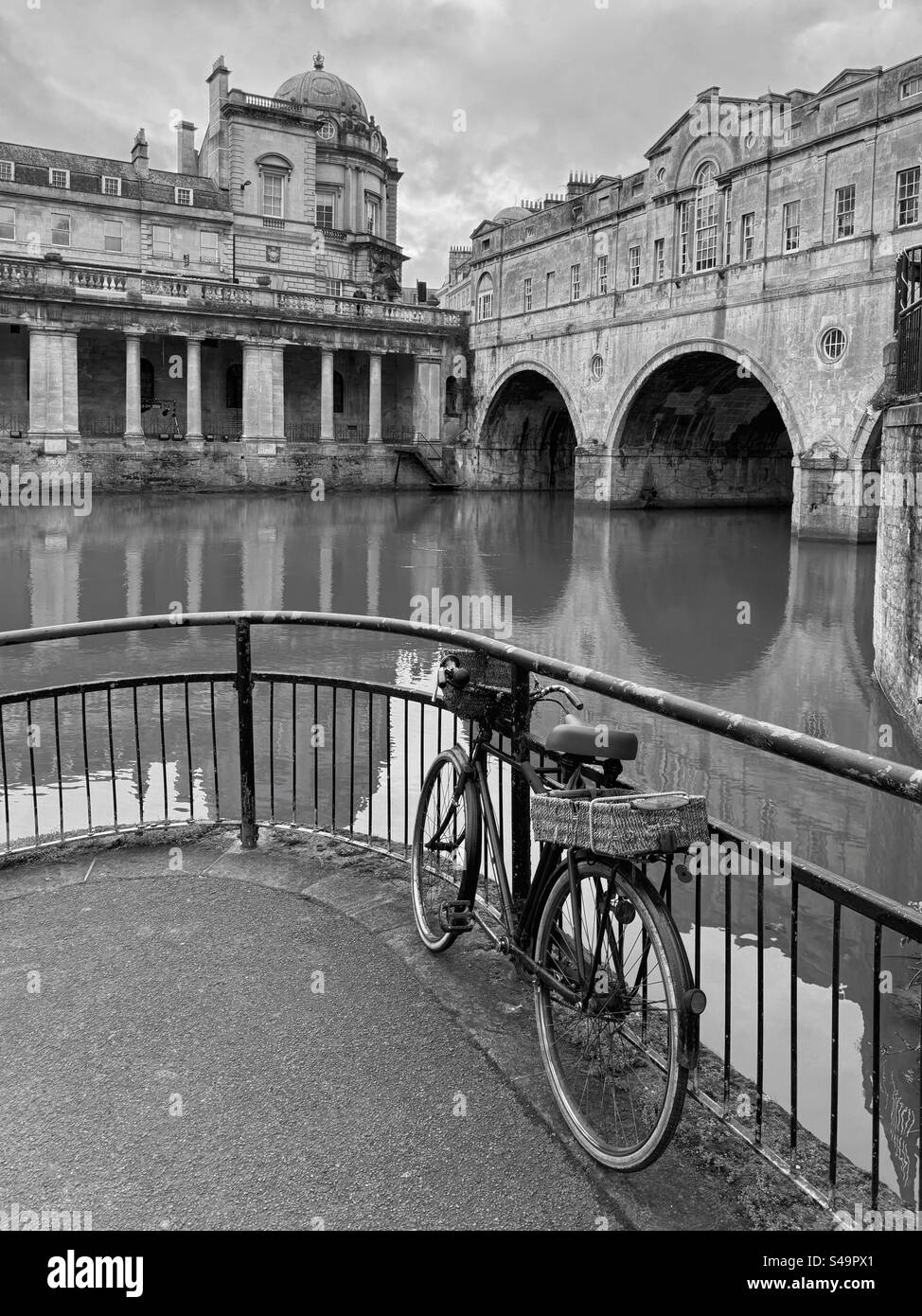 Un vélo isolé semble abandonné à côté de la rivière Avon et en face du célèbre pont Pultney à Bath, Somerset, en Angleterre. Photo ©️ COLIN HOSKINS. - Image de stock capturée avec un smartphone
