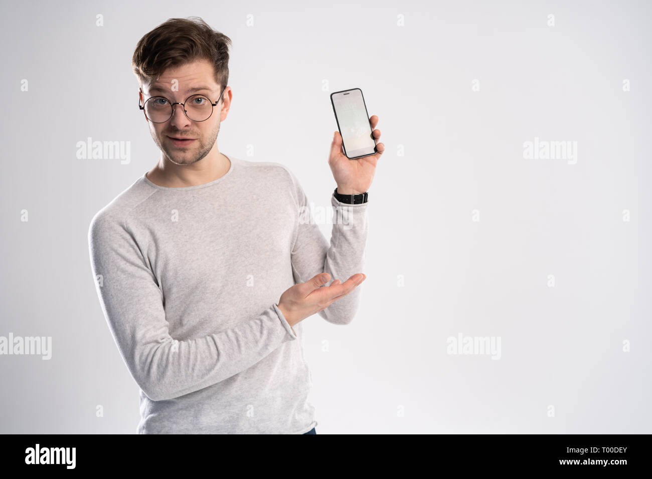 Portrait de jeune homme pointant avec son doigt sur l'écran de son smartphone sur fond blanc. Banque D'Images
