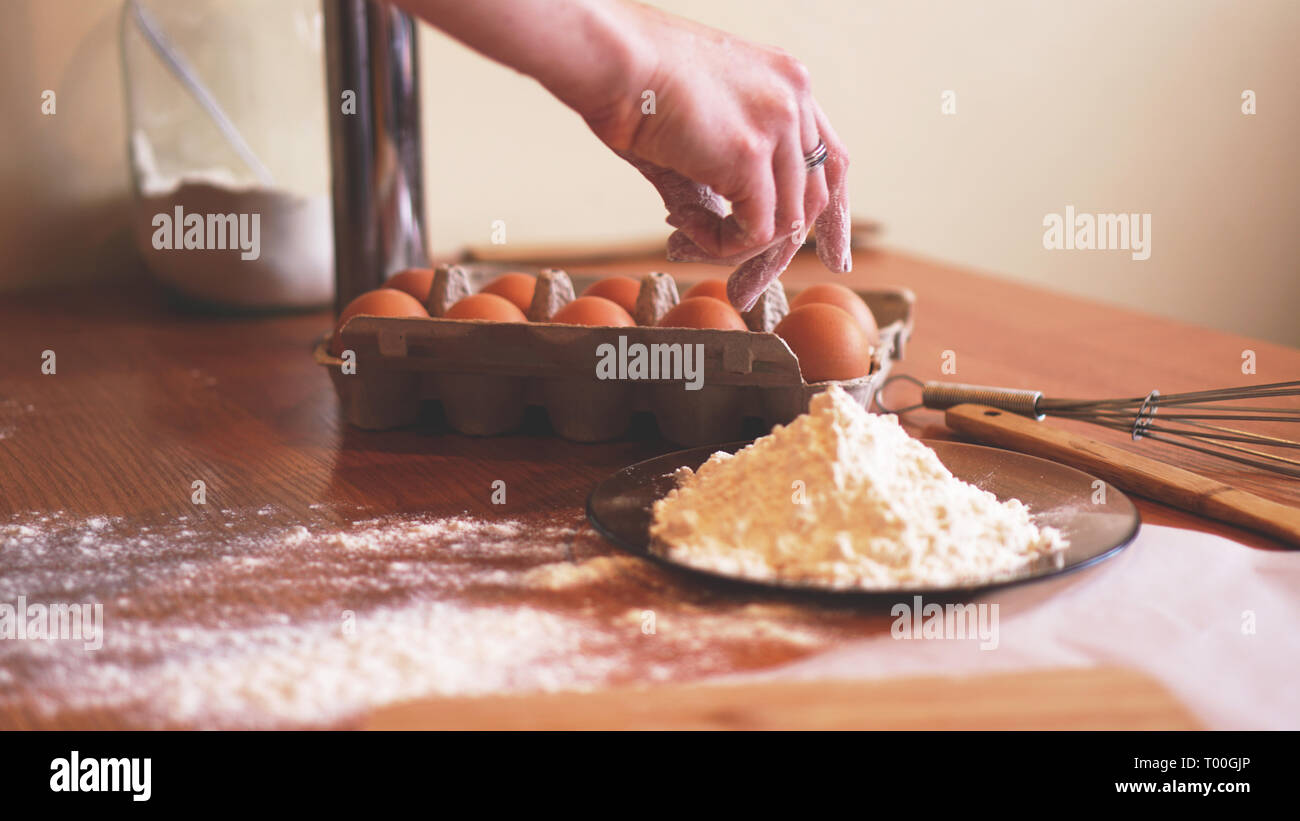 Les mains d'une femme chef choisir un oeuf pour faire de la pâte tandis que faire du pain avec un tas de blé à proximité Banque D'Images