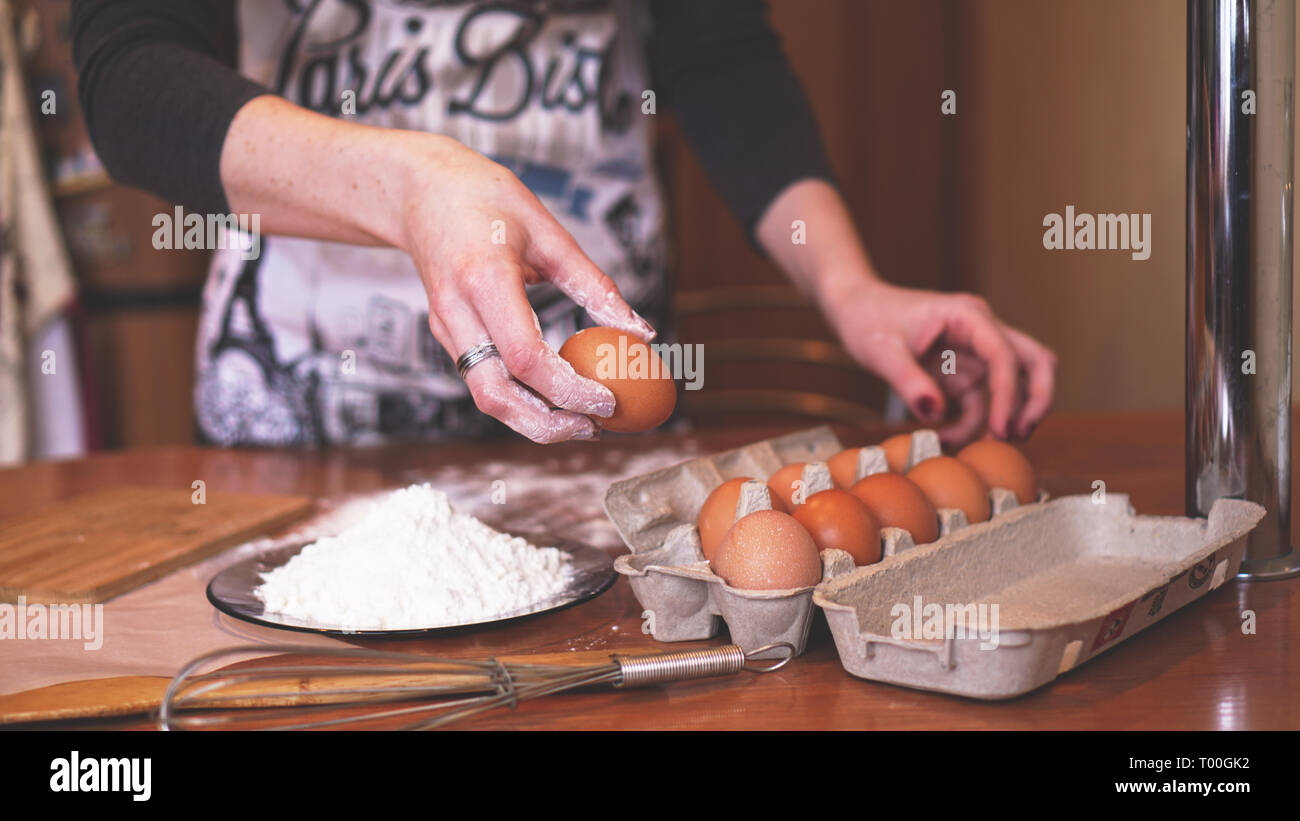 Les mains d'une femme chef choisir un oeuf pour faire de la pâte tandis que faire du pain avec un tas de blé à proximité Banque D'Images