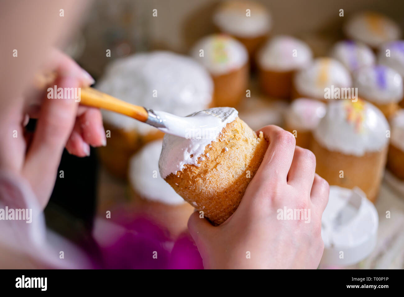 Brosses d'un boulanger un liquide sucre fouettée cerise sur le sommet d'un gâteau de Pâques traditionnel fabriqué à partir de pâte et cuit dans des formes cylindriques pour décorer les t Banque D'Images