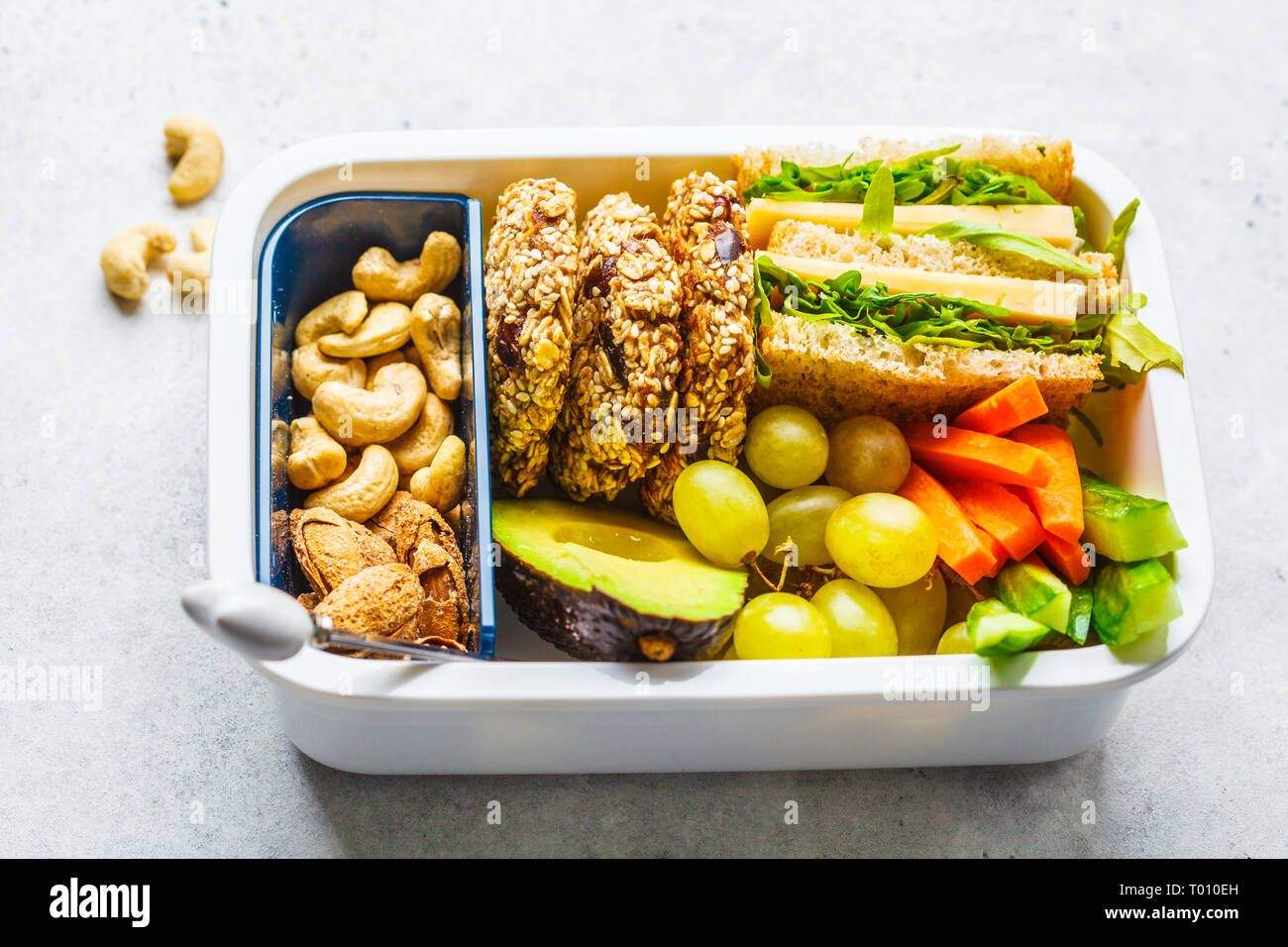 School healthy lunch box avec sandwich, des biscuits, des noix, des fruits et de l'avocat sur un fond blanc. Banque D'Images