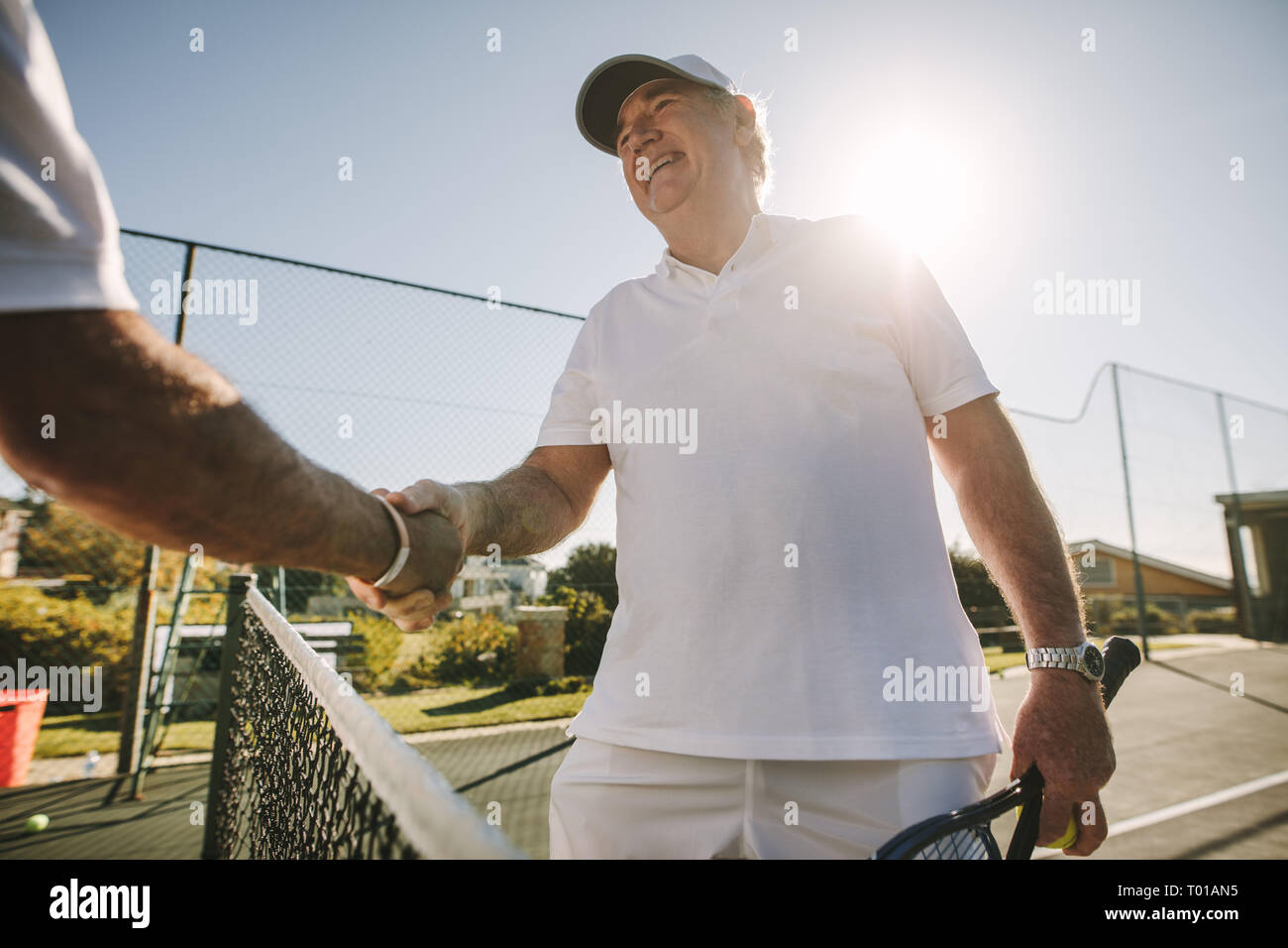 Man shaking hands debout sur un court de tennis. Accueil tennis player son adversaire debout près du filet avec le soleil en arrière-plan. Banque D'Images