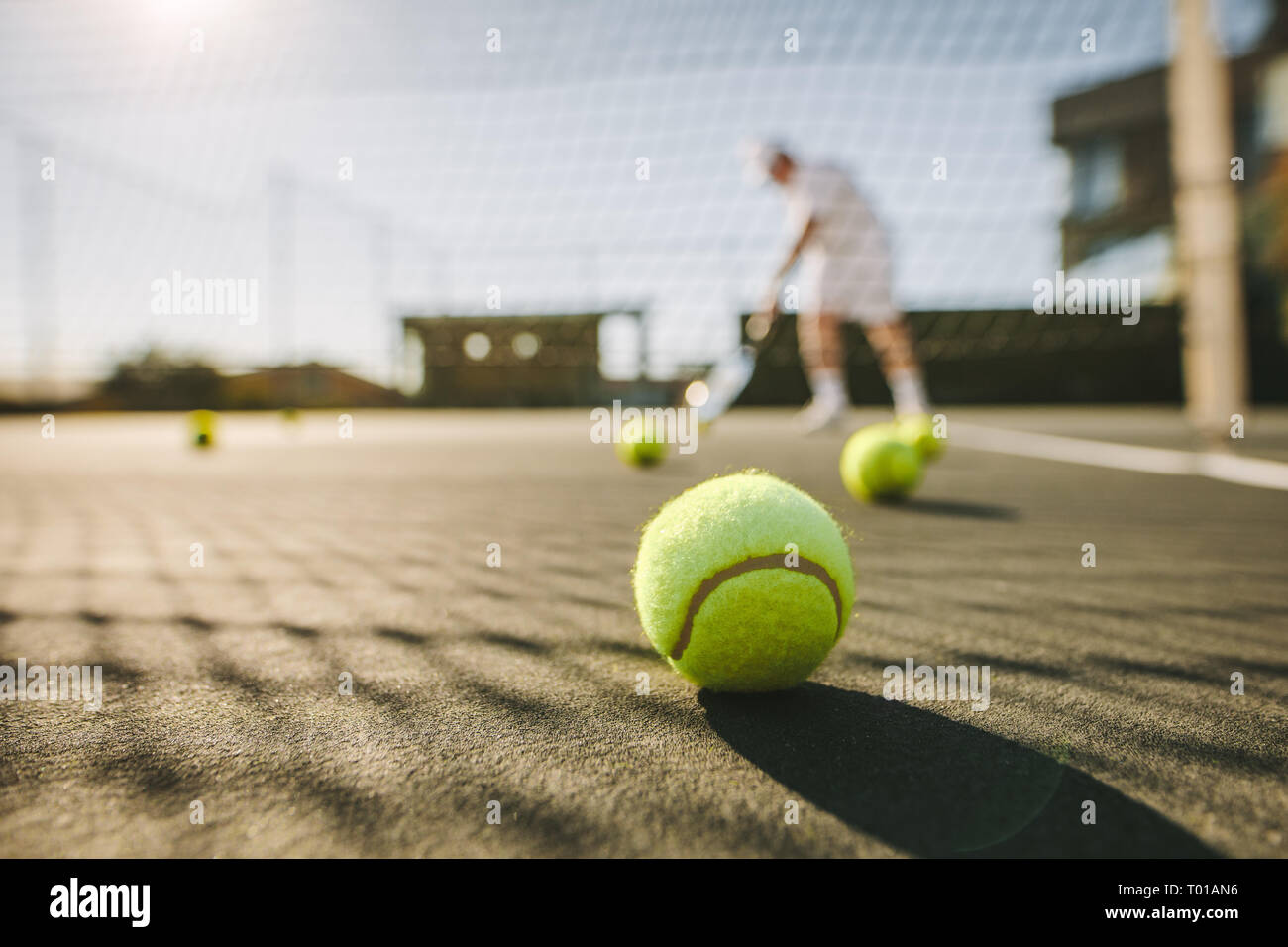 balles de tennis couchées au sol sur un court de tennis. Homme jouant au tennis par une journée ensoleillée avec des balles de tennis couchées sur le court. Banque D'Images