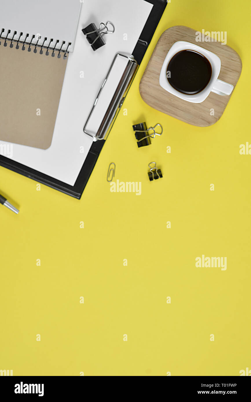 Des maquettes en blanc avec de l'espace de conseil clip, fournitures de bureau, stylo, tasse de café et les lunettes sur fond jaune. Mise à plat, vue du dessus Banque D'Images