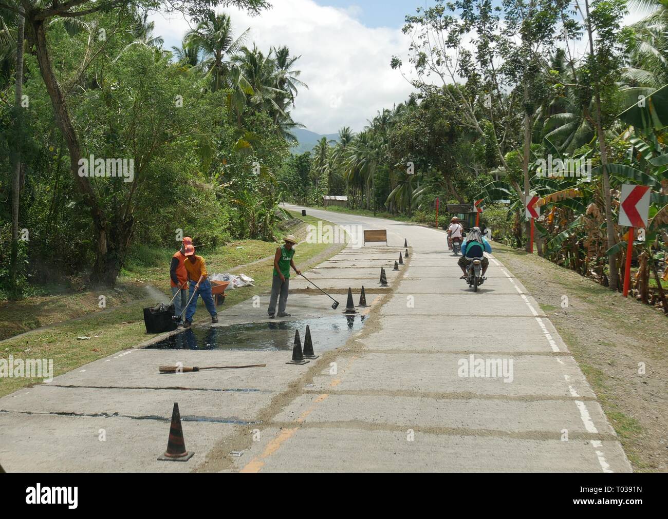 DAVAO ORIENTAL, PHILIPPINES—MARS 2016: Les travailleurs de la route effectuent des réparations sur la route nationale jusqu'à Davao Oriental, dans le sud des Philippines, par une bonne journée. Banque D'Images