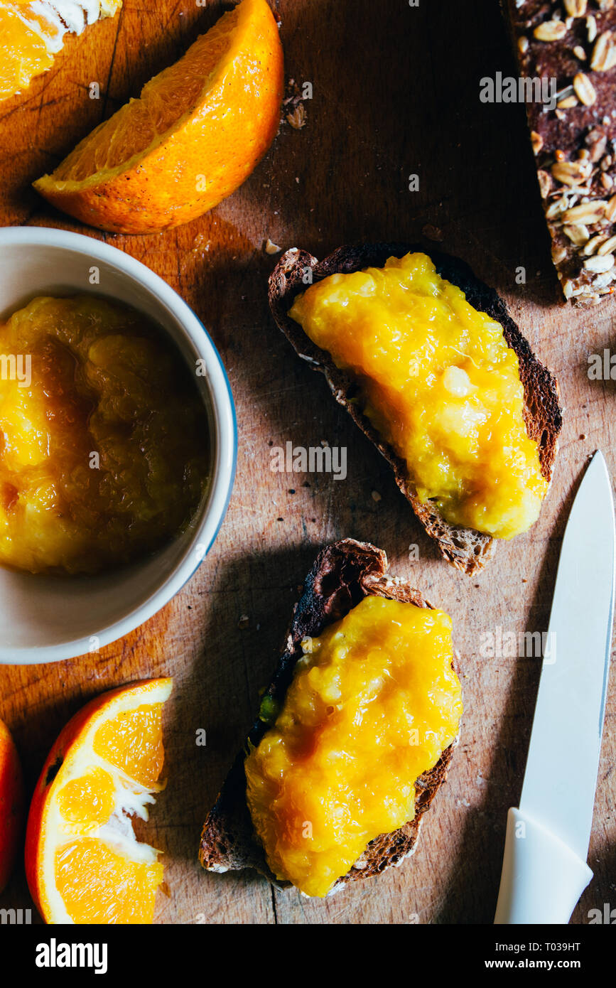 Confiture d'Orange fait maison sur un pain de blé de matières premières naturelles et les tranches d'orange sur une cutboard en bois, petit-déjeuner sain,close up et windom la lumière. Banque D'Images