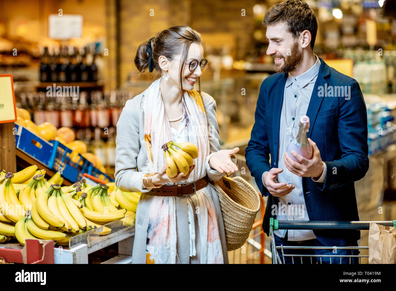 Jeune et beau couple qui achète la nourriture, le choix des fruits et du vin dans le supermarché Banque D'Images