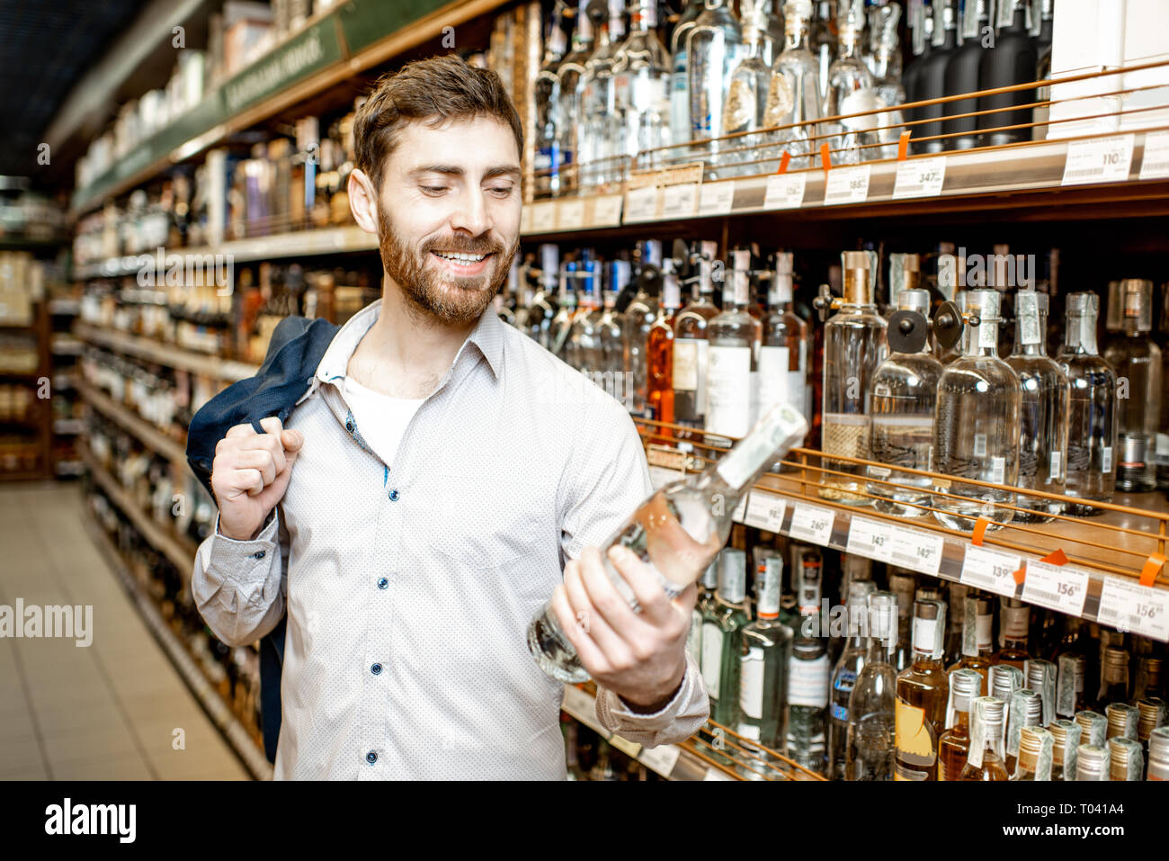 Portrait d'un homme avec une soif d'alcool, debout près de l'étagère avec des boissons fortes dans le supermarché Banque D'Images
