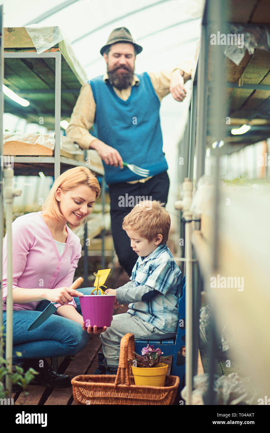 Notion d'éducation informelle. Garçon de planter des graines avec les parents. Cute kid holding hot pot rose et sa mère a couteau et papa porte fourche jardinage Banque D'Images