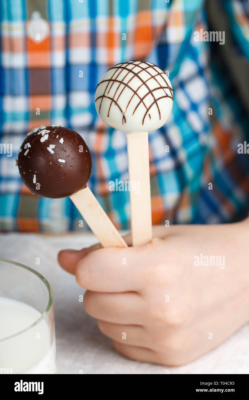 Deux cake pops décoré de chocolat blanc et noir dans les mains des enfants. Dessert pour les petits gourmets. Selective focus Banque D'Images