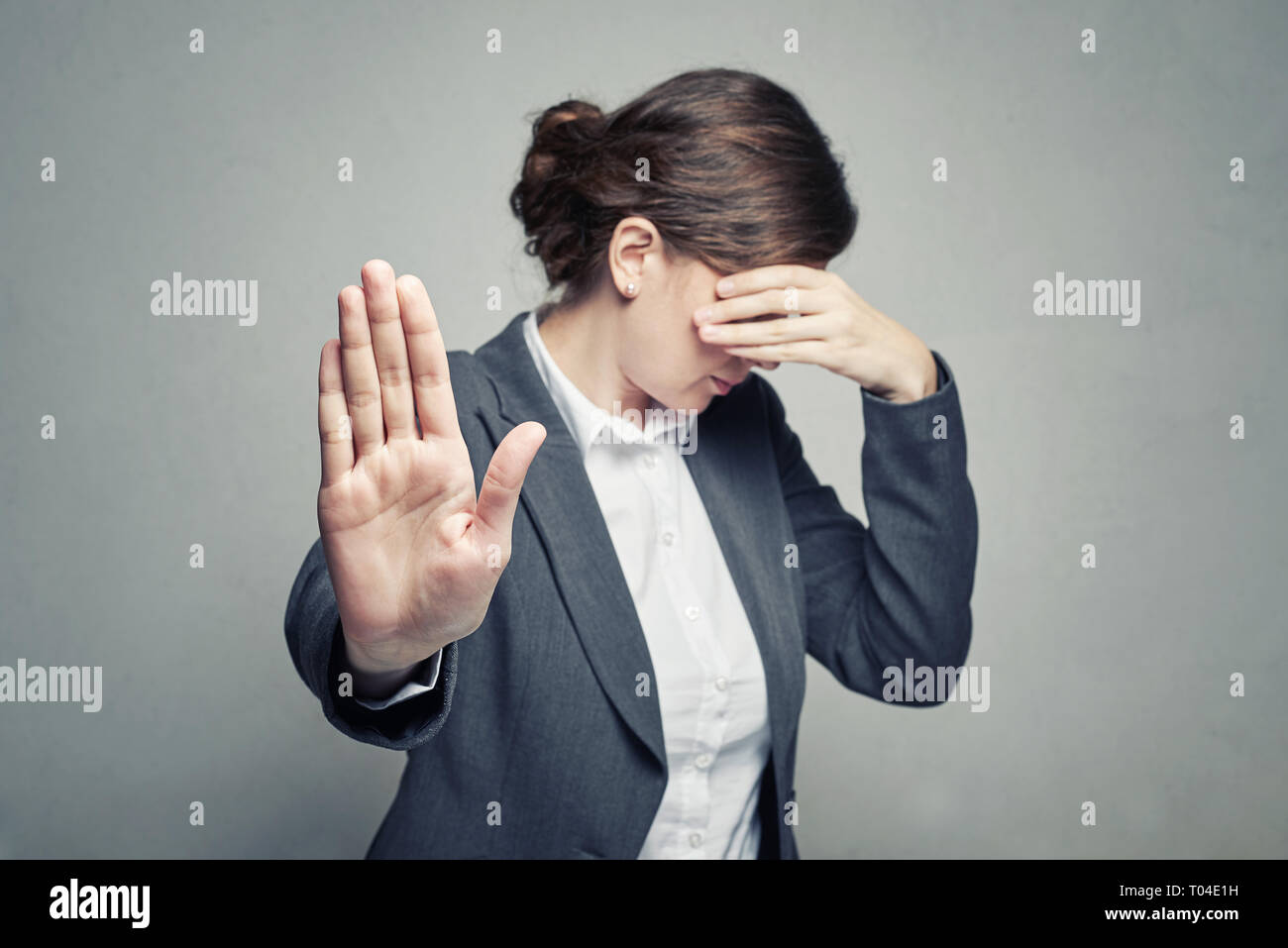 Femme en blouse et la fonction de couvrir son visage avec la main et montrer le geste d'arrêt sur fond gris Banque D'Images