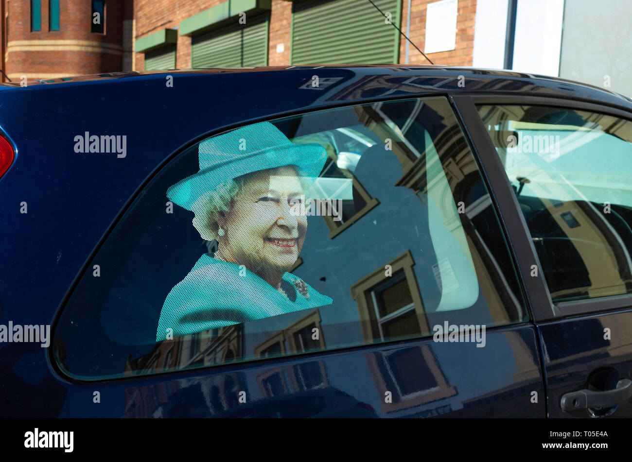 Photo de Sa Majesté la Reine sur la fenêtre arrière droite d'une petite voiture familiale Banque D'Images