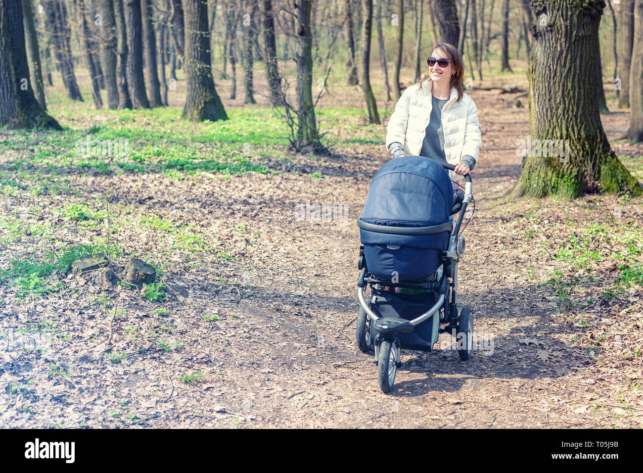 Belle jeune femme adulte balade avec bébé dans la poussette à travers la  forêt ou le parc. sur journée ensoleillée. Mode de vie sain et la santé des  enfants. Heureux Photo Stock -