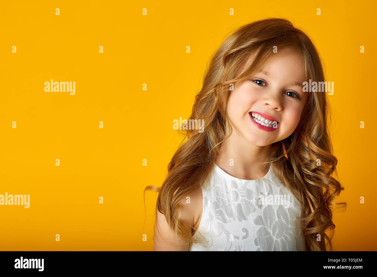 Jolie petite fille en robe est looking at camera and smiling while standing akimbo, isolé sur un fond jaune. Banque D'Images