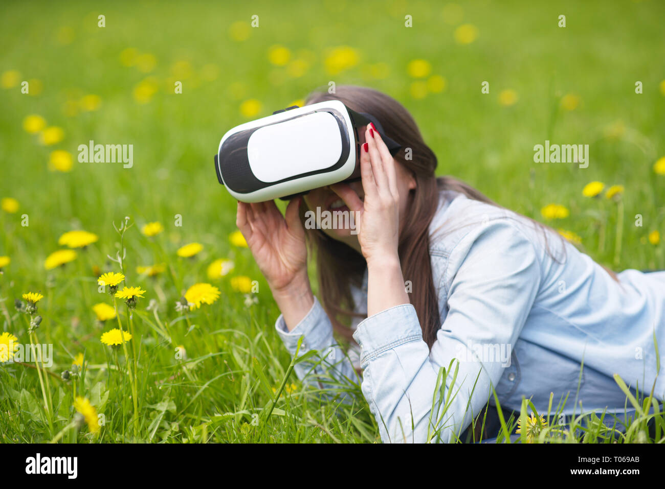 Femme à l'aide du casque de réalité virtuelle à l'extérieur pose en champ de fleurs de printemps Banque D'Images