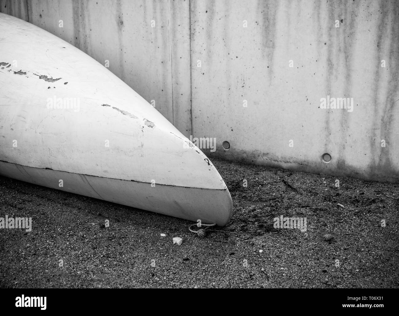 Kayak de plastique en fibre de verre blanc avec de marques avec cordon blanc sur la plage de sable noir avec des pierres en bord de mer près de mur de béton avec peo n Banque D'Images