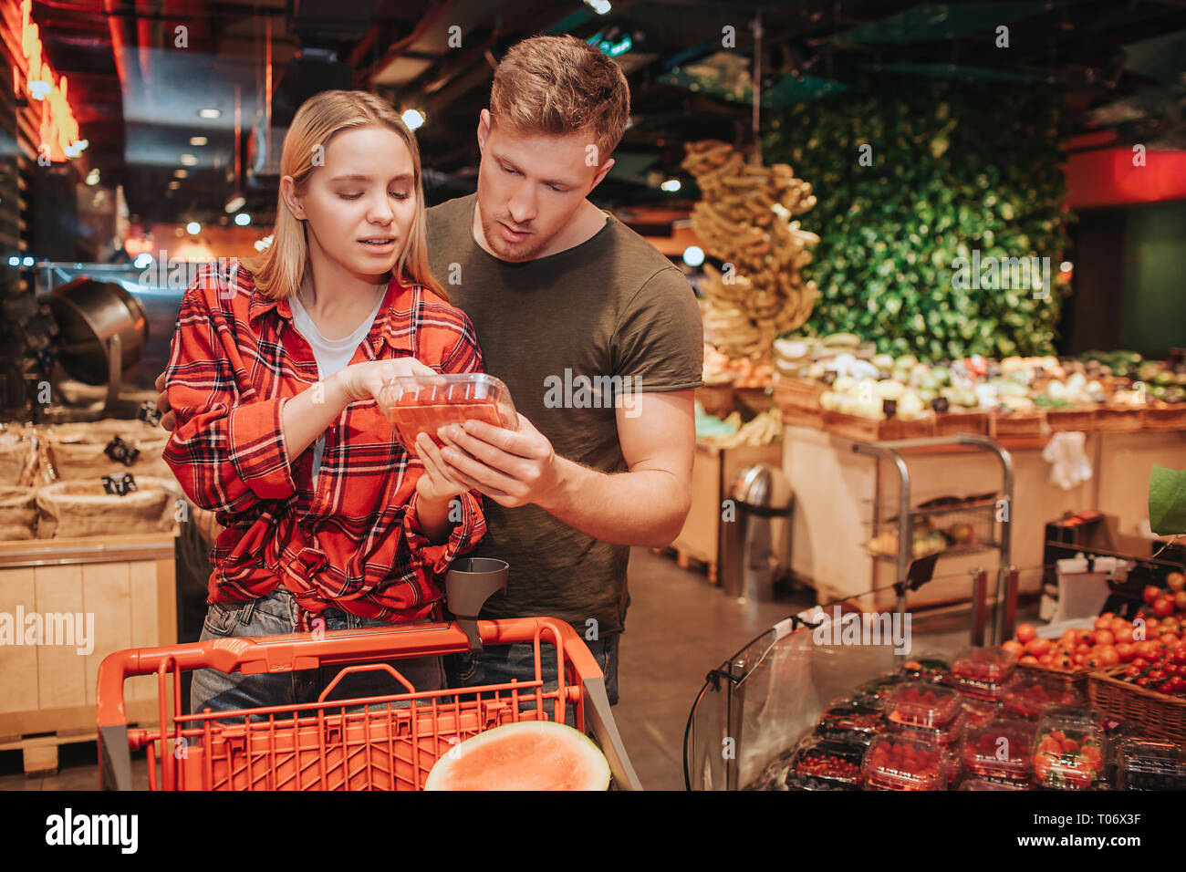 Jeune couple en épicerie. Ils se tiennent ensemble et lire le texte sur la plaque des petits fruits. Chariot avec en face de l'épicerie de couple. Concentré grave Banque D'Images