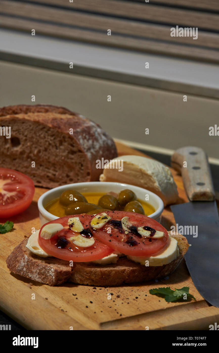 Pain au levain de seigle avec tomates mozzarella olives et rustique avec vue latérale du couteau avec un peu de lumière naturelle Banque D'Images