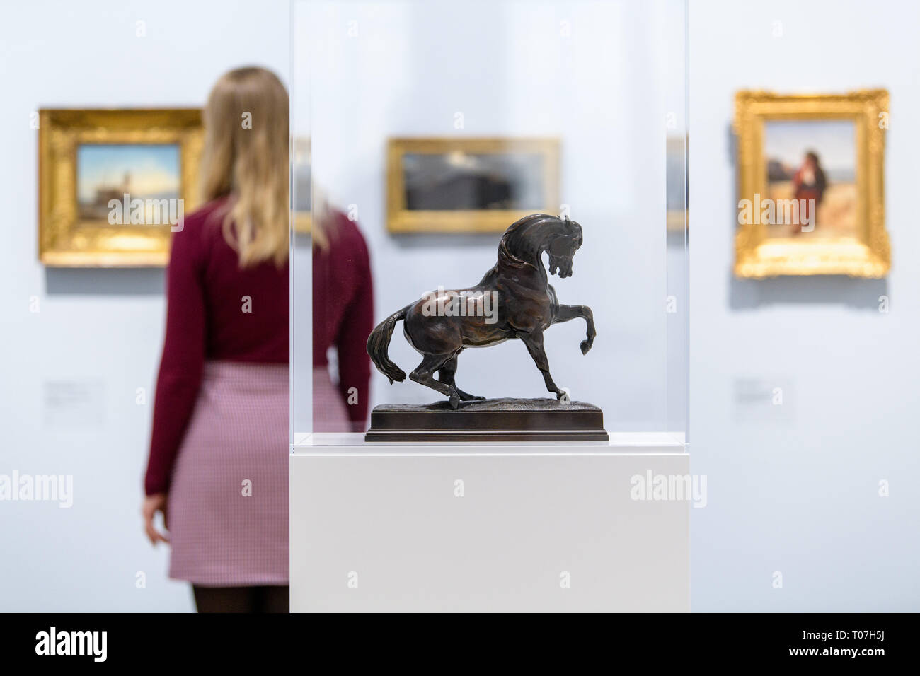 18 mars 2019, Bavaria, Munich : le modèle 'bronze' Cheval Turc par Antoine-Louis Barye (ca. 1835/1840) peut être vu dans l'exposition "Nature comme de l'Art - Paysage au 19e siècle, dans la peinture et la photographie' dans la Städtische Galerie in Lenbachhaus, tandis qu'une femme est à la recherche de peintures dans l'arrière-plan. Les œuvres des collections de la Fondation Christoph Heilmann et le Musée de la ville de Munich sera à l'exposition à partir de 19.03. à 18.08.2019. Photo : Matthias Balk/dpa Banque D'Images