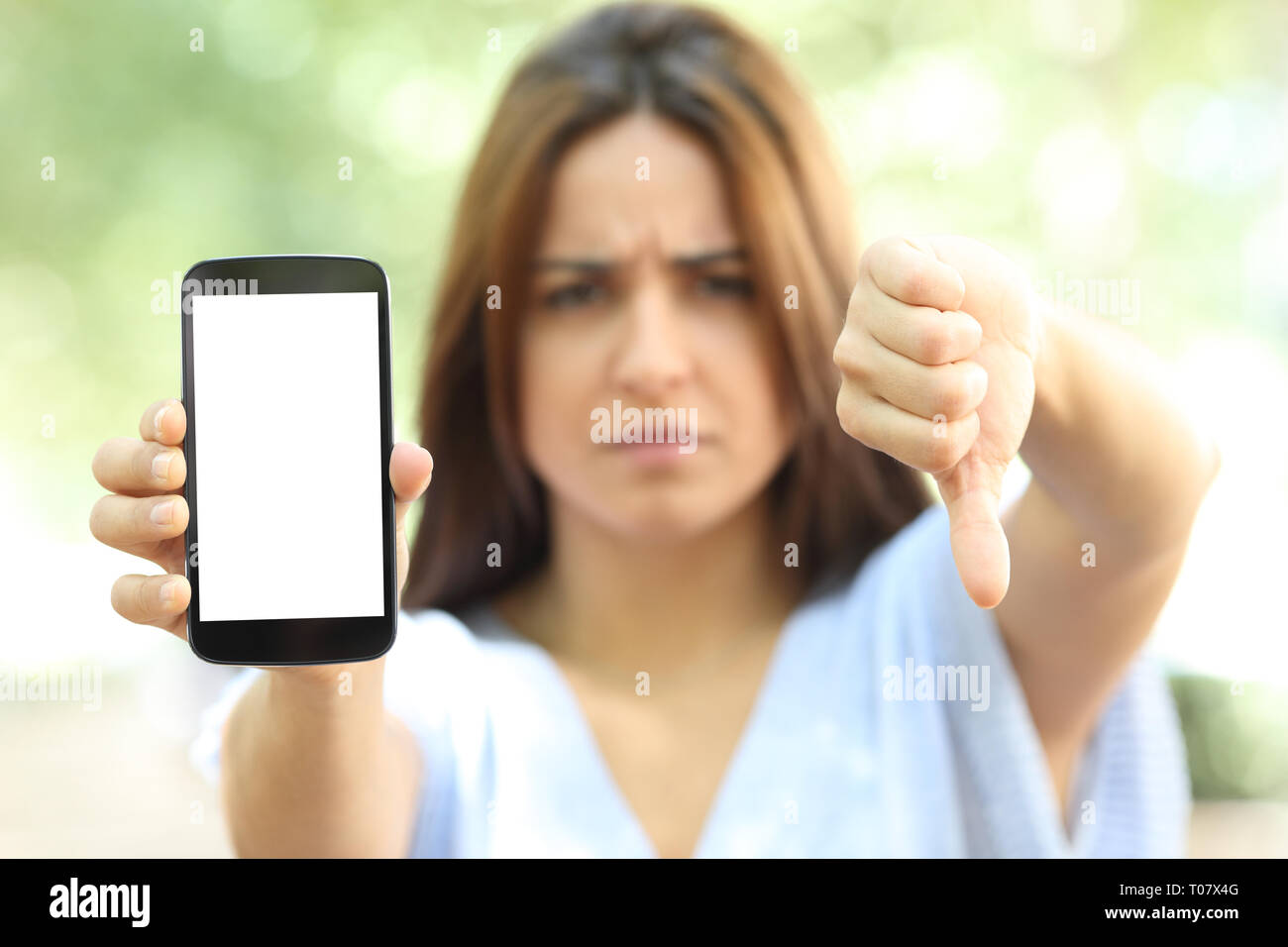 Vue avant portrait de femme en colère montrant smart phone écran blanc avec le pouce vers le bas dans la rue Banque D'Images