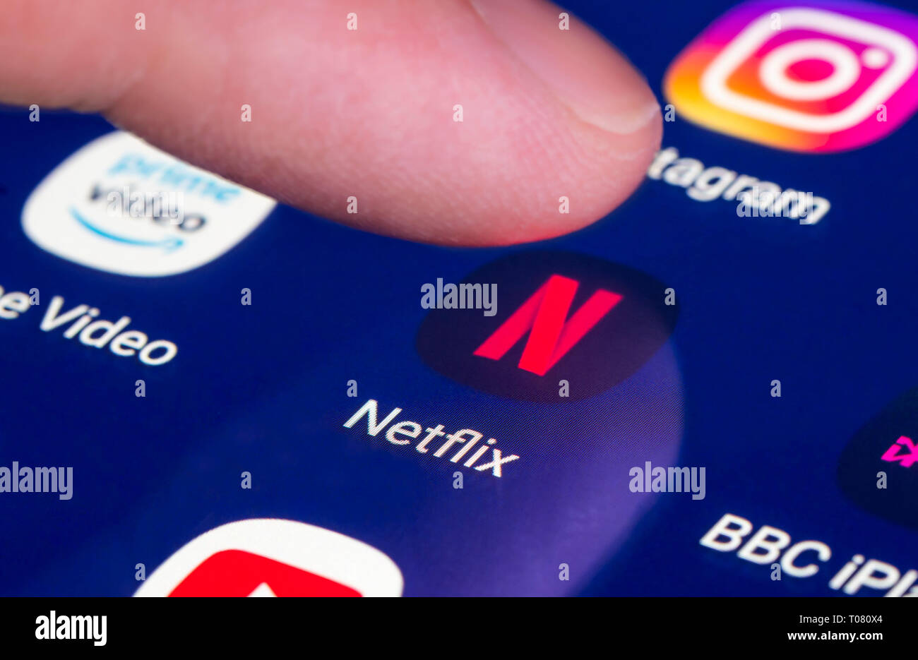 Doigt qui appuie sur l'icône app Netflix sur un écran tactile sur une tablette ou un téléphone mobile. Le chargement de l'application Netflix. Raccourci de Netflix. Banque D'Images