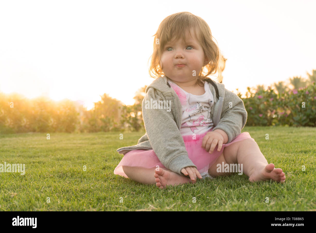 Funny little girl sitting on grass en vacances Banque D'Images