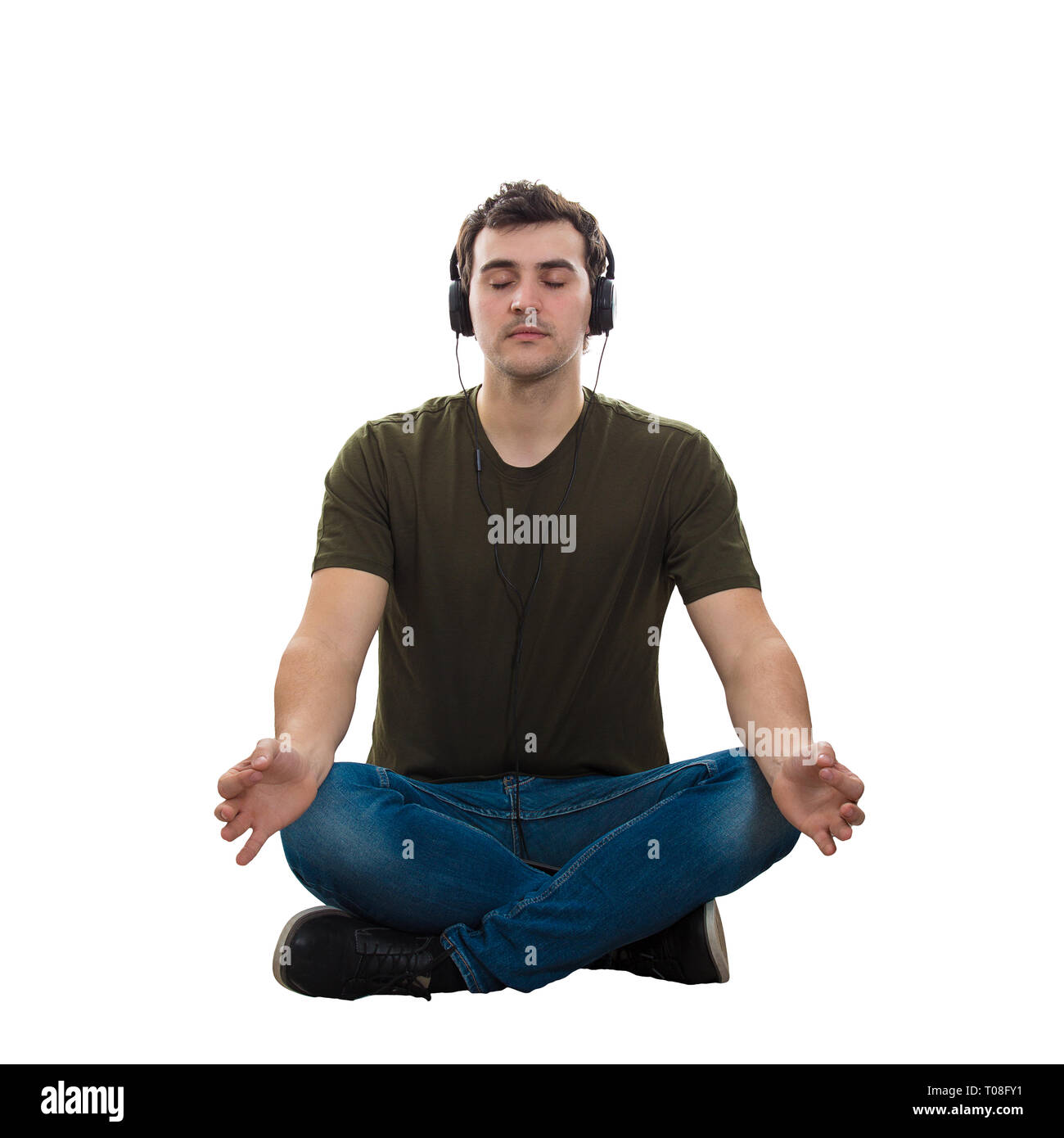 Casual homme assis sur le sol les yeux fermés et les jambes croisées, les mains montrant le zen geste comme pratiquant le yoga tout en écoutant de la musique sur earphon Banque D'Images