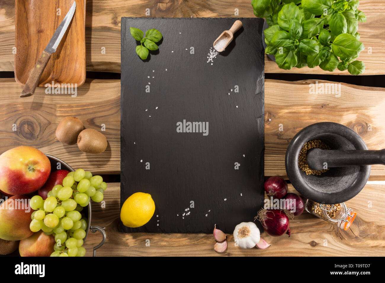 Serveur d'Ardoise/Conseil/plateau avec espace pour texte sur planches de bois rustique. Organisé les fruits, ail, oignons, sel, scoop et feuilles de basilic. Banque D'Images