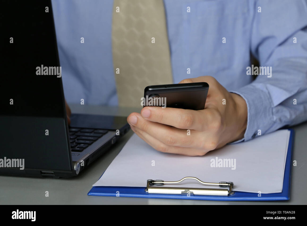Le travail de bureau, l'homme en chemise bleue et cravate assis à une table avec un ordinateur portable. Les mains des hommes de taper au clavier, en utilisant smartphone, concept de manager, greffier Banque D'Images