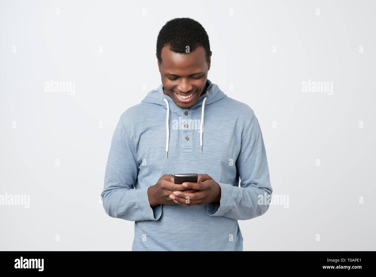 Jeune homme africain à l'aide de téléphone mobile chatter dans internet avec ses amis. Banque D'Images