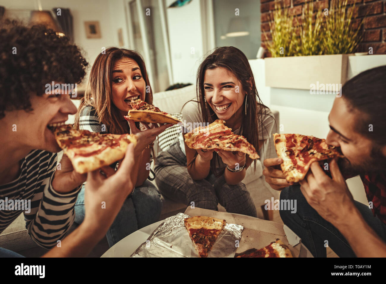 Amis est excité à la maison assis sur un canapé. Amener leurs amis à pizza manger ensemble. Elles ont un grand week-end à Nice à l'intérieur de l'entreprise. Banque D'Images