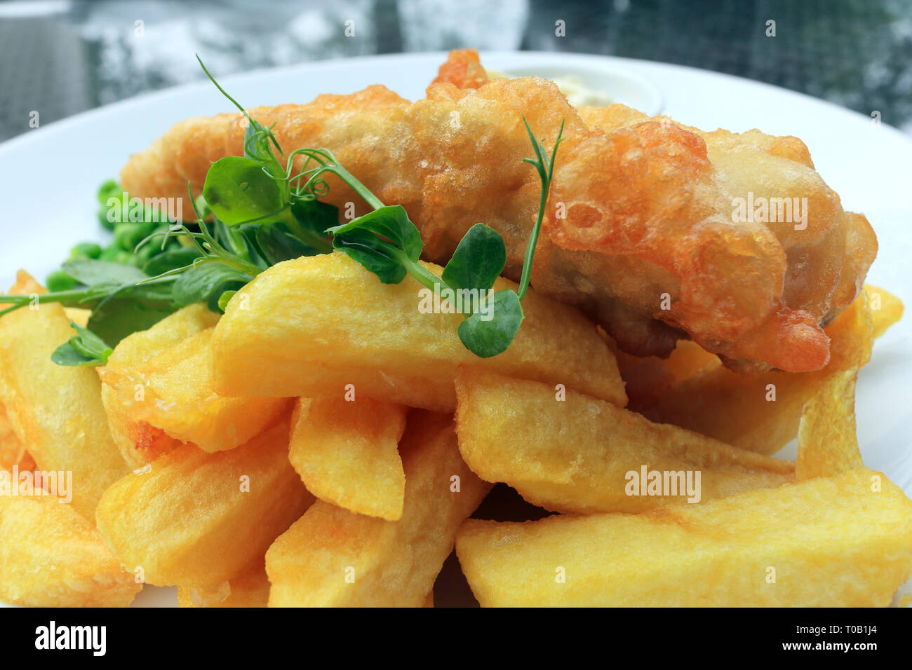 Des plats anglais traditionnels de cod fish and chips, garnie de verts, servi sur une plaque blanche. Banque D'Images