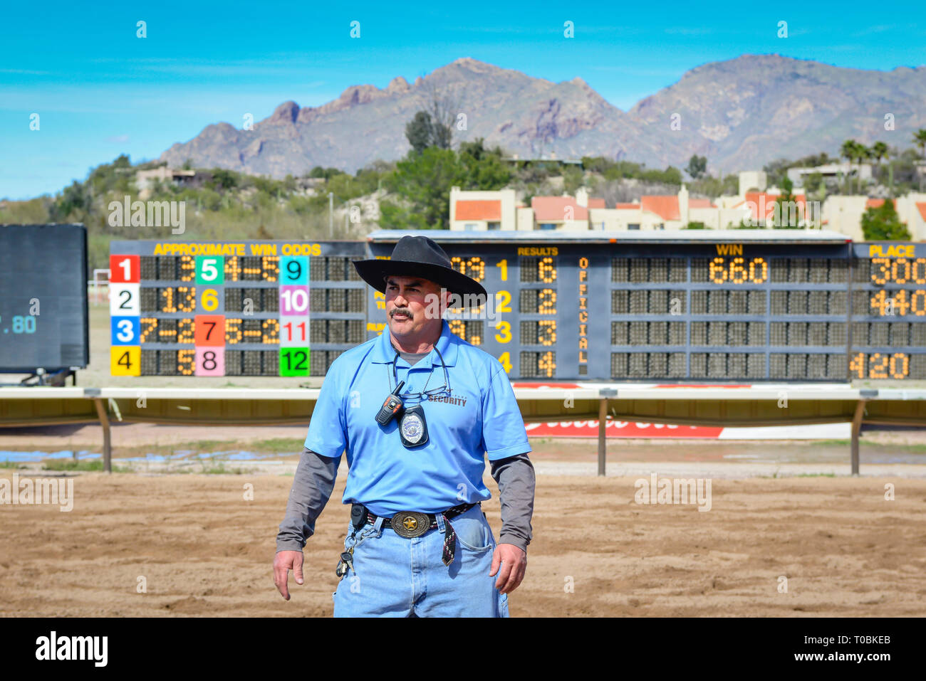 Un homme moustachu portant un chapeau de cow-boy est à la sécurité de Rillito Park Racetrack debout devant le tableau d'affichage à Tucson, AZ Banque D'Images