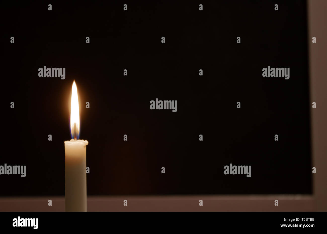 Burning candle burns blanc sur fond noir. Le deuil, la tristesse, la tristesse. Situé sur la gauche. Il y a une place pour votre texte. Banque D'Images