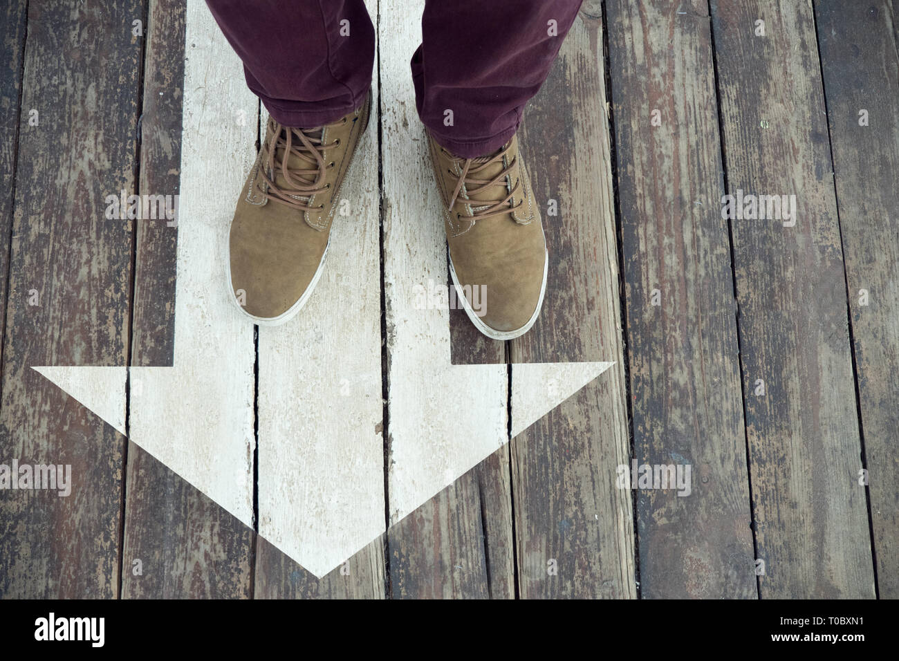 Flèche blanche signe sur un plancher en bois. Les jambes de l'homme debout sur panneau de flèche peinte sur le sol. Direction l'arrière-plan. Recherche de fond. Guidline Banque D'Images