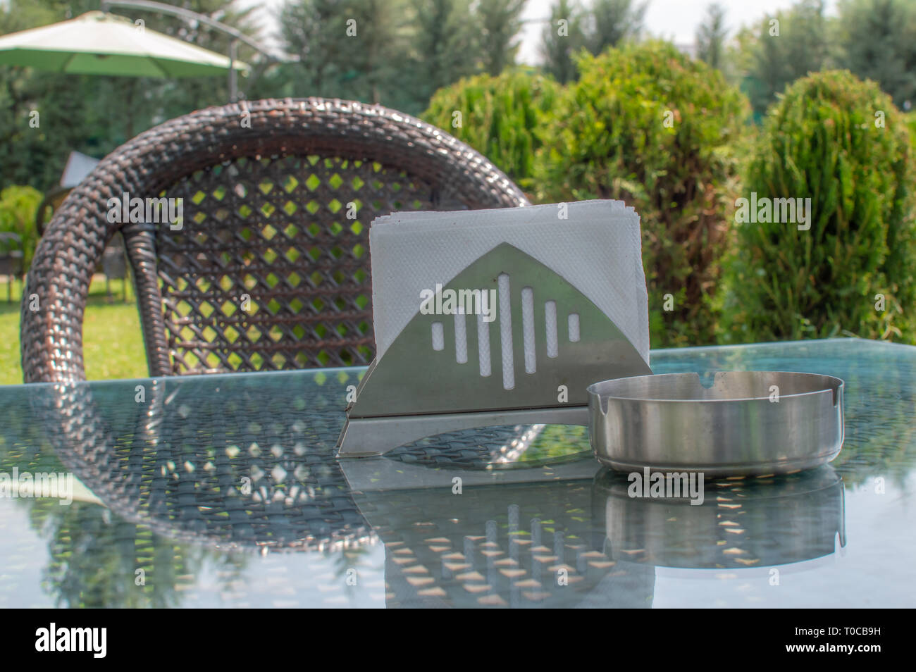 Une chaise avec une table et cendrier sur la table en verre dans un café avec ses plantes vertes luxuriantes Banque D'Images