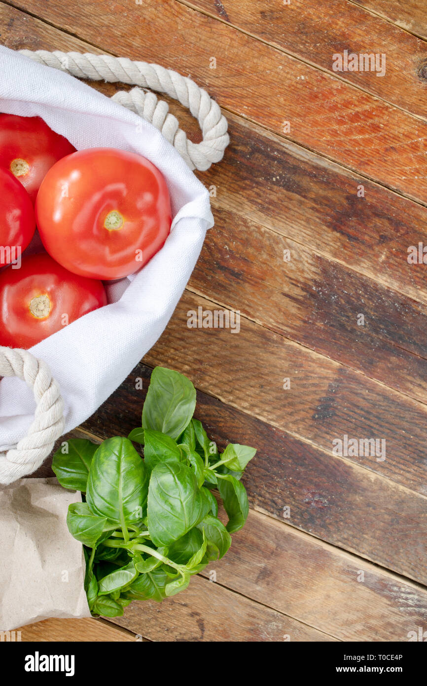 Tomates mûres rouge et vert basilic dans des emballages écologiques sur la diagonale table en bois. Banque D'Images