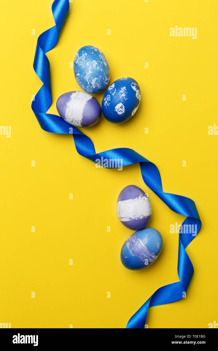 Les oeufs de Pâques multicolores de fête avec du ruban bleu sur fond jaune. Bleu, Violet et violet oeufs poulet bouilli avec ruban bleu. Concept d'Easte Banque D'Images Les oeufs de Pâques multicolores de fête avec du ruban bleu sur fond jaune. Bleu, Violet et violet oeufs poulet bouilli avec ruban bleu. Concept d'Easte Banque D'Images