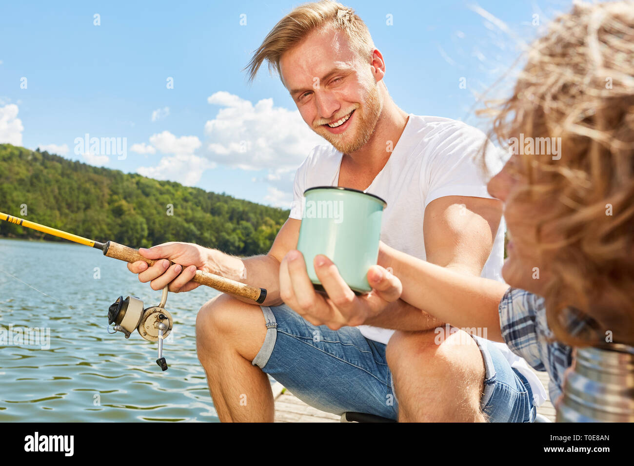 Garçon donne son père une tasse de café pendant la pêche au lac sur le week-end Banque D'Images Garçon donne son père une tasse de café pendant la pêche au lac sur le week-end Banque D'Images