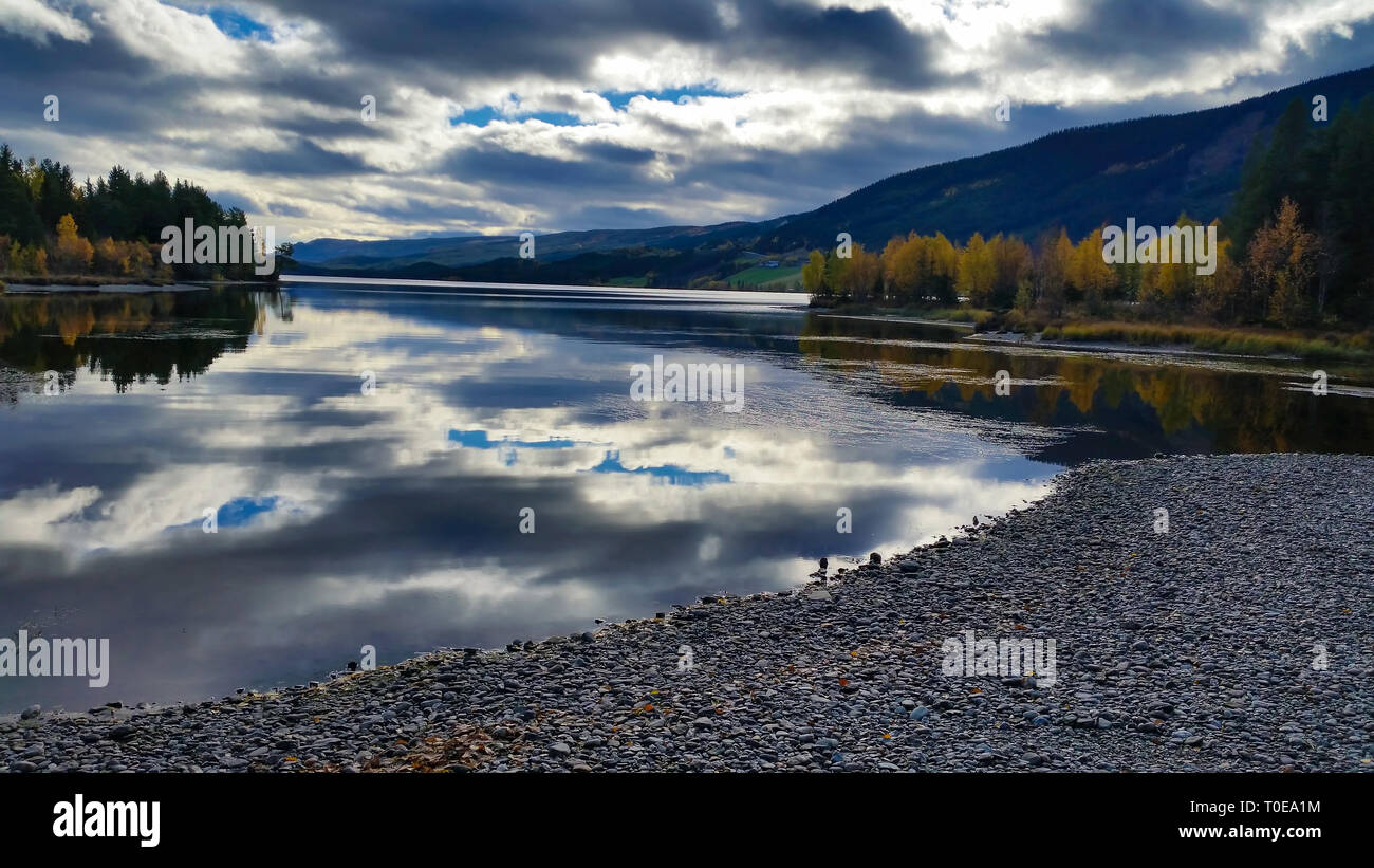 Calme et paisible paysage intact décor de plage de galets et lac avec nuages spectaculaires reflétées dans l'eau calme avec des arbres autour de l'automne Banque D'Images