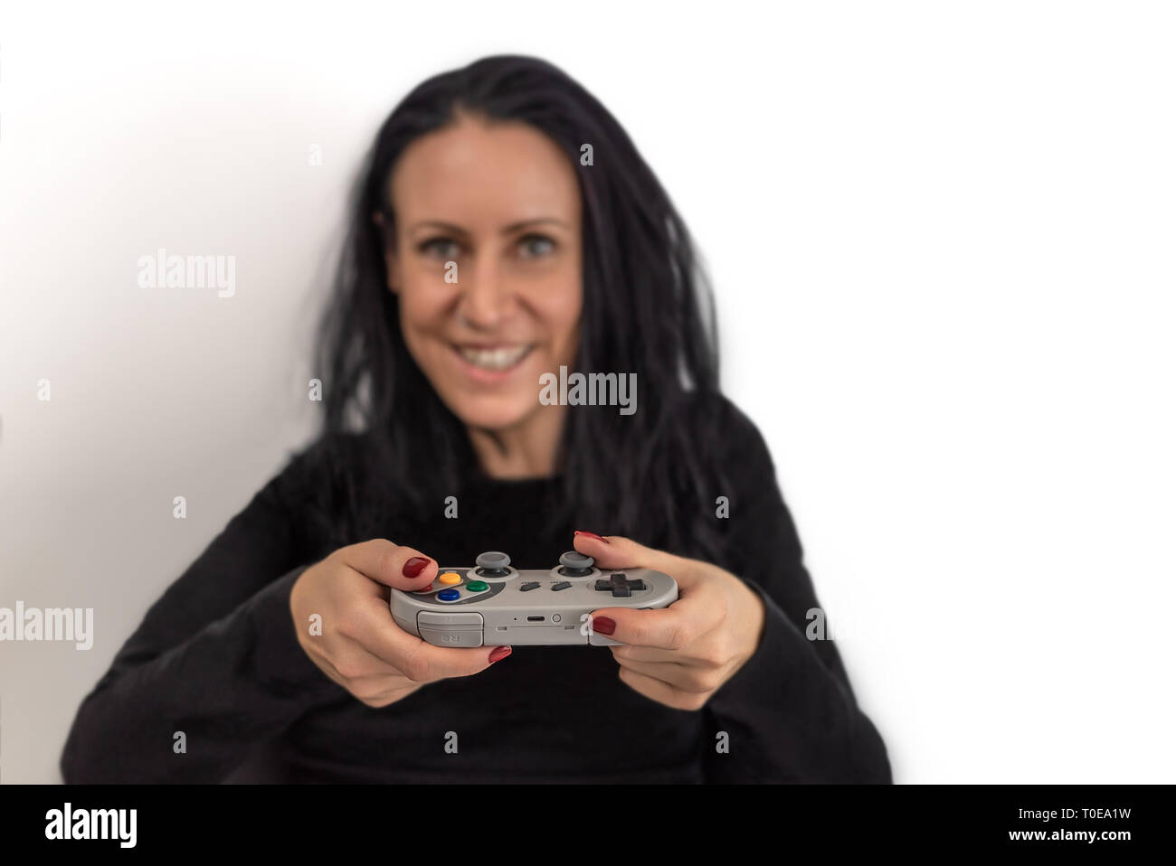 Jeune femme avec du vernis à ongles rouge playing video game sur un contrôleur de jeu sans fil rétro avec un heureux et concentré d'expressions du visage Banque D'Images
