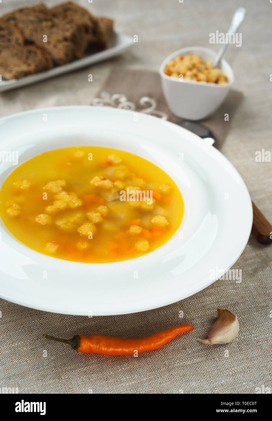 Soupe au poulet avec des légumes dans un bol blanc avec des croûtons de pain et craquelins de poivre sur nappe. Banque D'Images