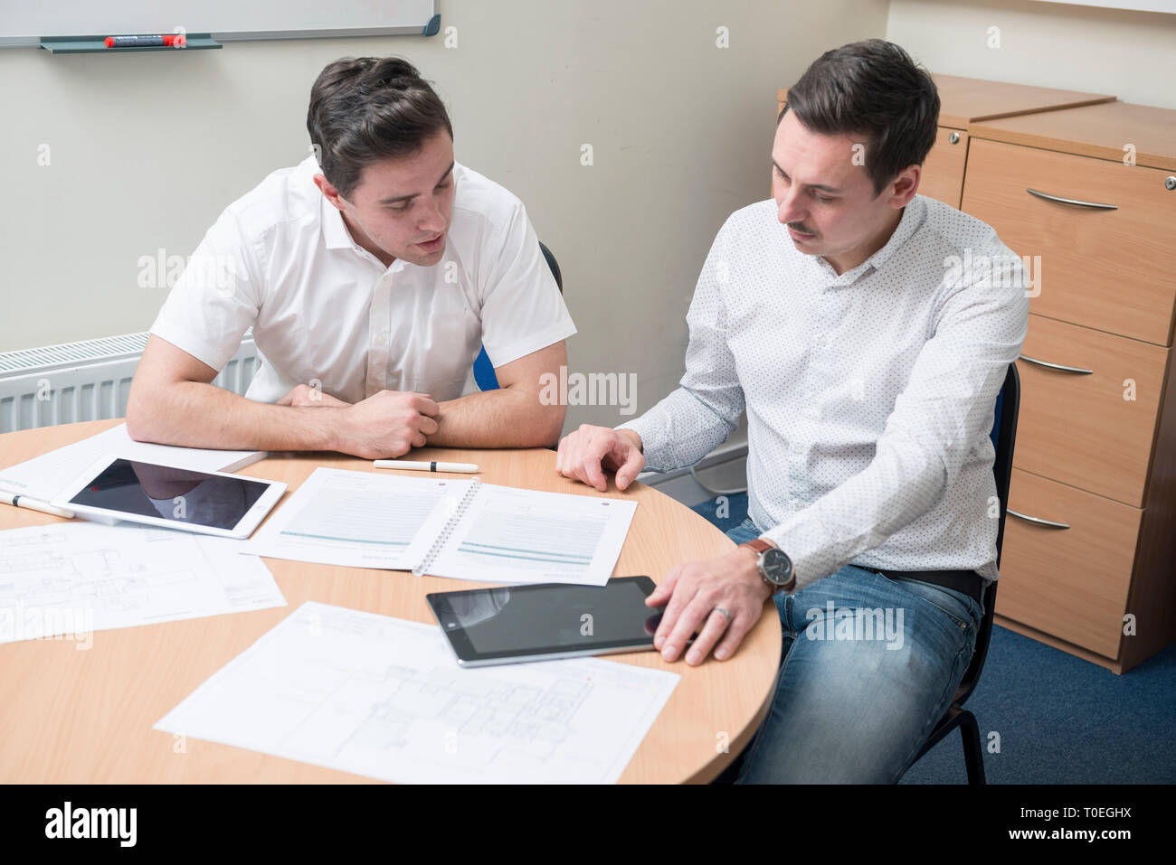 Deux hommes assis autour d'une table dans une petite salle de réunion du bureau de réviser les plans dans un entretien de vente Banque D'Images