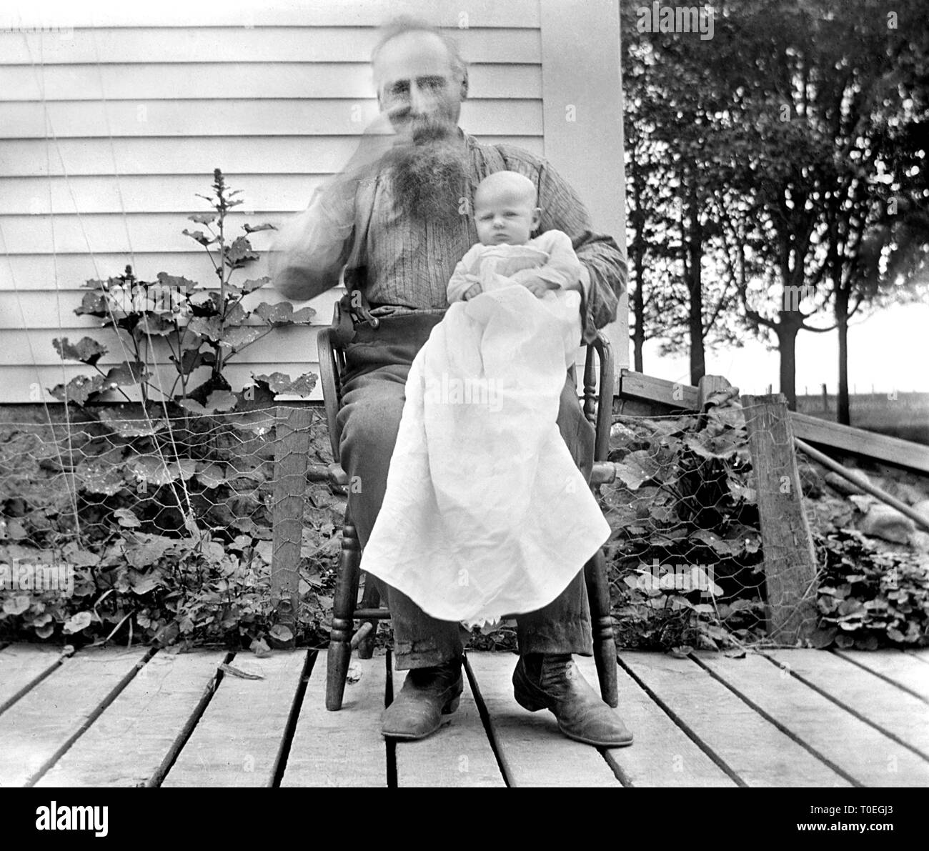 Grand-père ne peut rester en place et des rayures son nez pendant un temps d'exposition photographie avec son nouveau petit-fils, baptisé ca. 1900. Banque D'Images