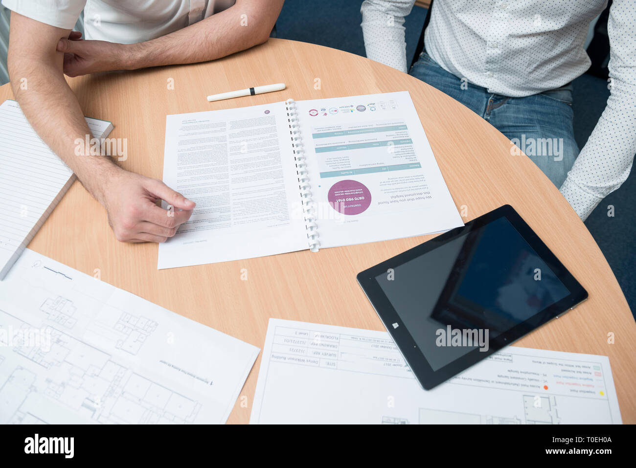 Deux hommes assis autour d'une table dans une petite salle de réunion du bureau de réviser les plans dans un entretien de vente Banque D'Images