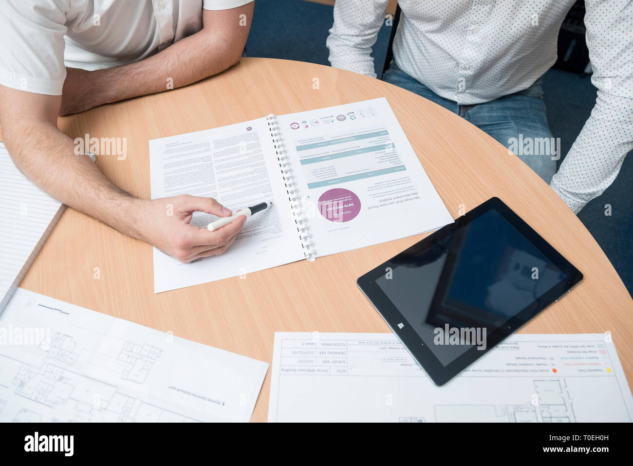 Deux hommes assis autour d'une table dans une petite salle de réunion du bureau de réviser les plans dans un entretien de vente Banque D'Images
